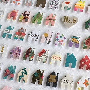 May include: A collection of small, die-cut paper house shapes featuring diverse patterns, colours, and illustrations. Some houses display text including 'LUCK', 'Cosy', 'PAWFECT', 'SOLD', and 'love', alongside a heart-shaped piece labelled 'No.6'.