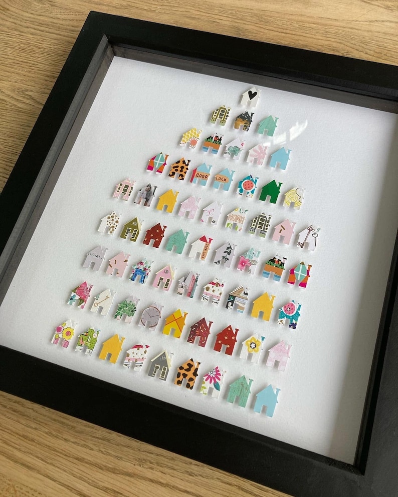 May include: A framed wall art piece featuring a collection of small, house-shaped cutouts arranged in a triangular tree formation. Each individual house cutout displays a unique pattern, colour, or graphic design, including floral, geometric, and text prints.