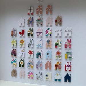 May include: A collection of small house-shaped paper cutouts arranged in a grid on a white surface. The houses feature various colourful patterns, floral prints, and geometric designs. Some houses display the text 2024, ABI & GARIN, and THYME CLOSE.