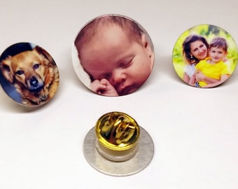 May include: Three round, silver-colored pins with different images printed on them. The first pin features a dog, the second pin features a baby, and the third pin features a mother and child. The pins have a gold-colored back.