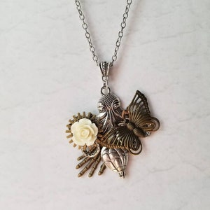 Peut inclure: Un collier avec une chaîne argentée et un pendentif orné d'une fleur blanche, d'un papillon et de divers breloques en métal de style steampunk.