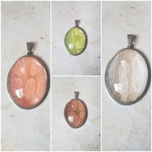 Può includere: Tre ciondoli di forma ovale con cornici argentate e diversi motivi colorati all'interno. I ciondoli sono su uno sfondo bianco.