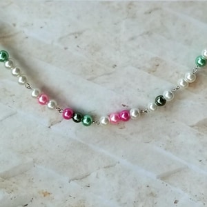 Op de afbeelding: Een zilveren ketting met witte, roze en groene parels.