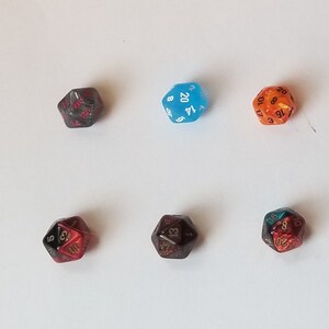 May include: Six different colored twenty-sided dice with black numbers. The dice are on a white surface.