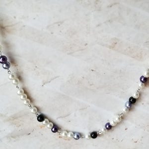 May include: A silver chain necklace with white, black, and purple beads.