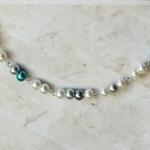 May include: A silver chain necklace with white and blue pearls. The pearls are interspersed with silver and dark blue beads.