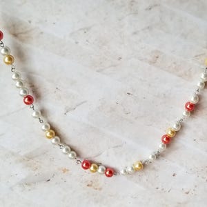 Könnte beinhalten: Eine silberne Kettenkette mit weißen, goldenen und roten Perlen.