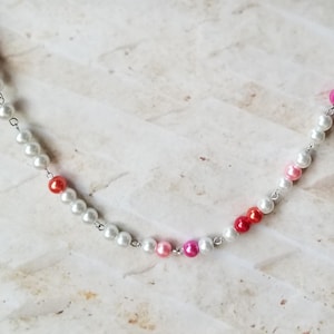 May include: A delicate silver chain necklace with white pearls and red, pink, and orange accents.