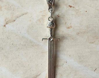 May include: Silver-toned sword pendant necklace. The pendant features a detailed sword design with a textured handle and a chain. The necklace is displayed against a neutral background.
