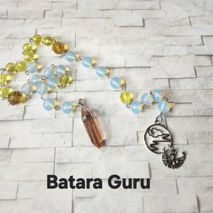 May include: A beaded chain featuring alternating translucent light blue and faceted yellow beads, accented with a brown crystal point pendant and a silver-toned circular charm depicting a cloud and mountain range, with the text Batara Guru below.