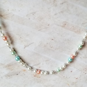 Könnte beinhalten: Eine zarte Halskette mit einer silbernen Kette und Perlen in Pastellfarben. Die Perlen sind eine Mischung aus Weiß, Hellblau und Hellrosa.