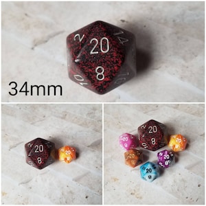 Puede incluir: Primer plano de un dado de 20 caras rojo y negro con números blancos. El dado tiene 34 mm de diámetro. El dado está rodeado de otros dados de diferentes colores.