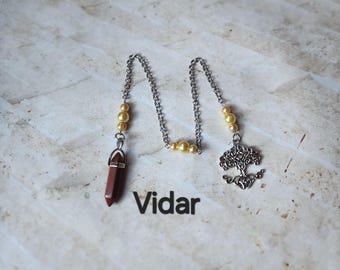 Puede incluir: Un marcapáginas de cadena plateada con un colgante de cristal marrón y un dije de árbol de la vida plateado. La cadena tiene cuentas doradas. La palabra "Vidar" está impresa en negro.
