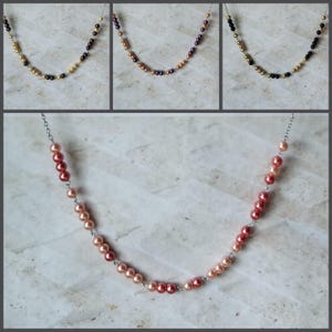 May include: Three necklaces with different colored beads. The first necklace has gold and black beads. The second necklace has gold and purple beads. The third necklace has gold and black beads. The fourth necklace has a gradient of pink and red beads.