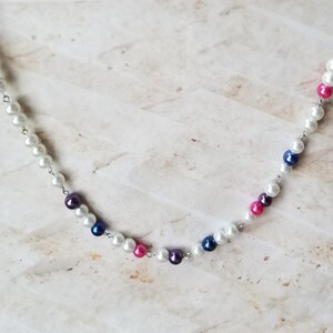 May include: A silver chain necklace with white, pink, and blue pearl beads.