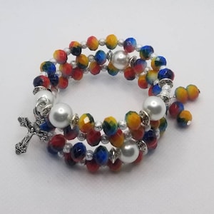 May include: A multi-strand bracelet with red, yellow, blue, and white beads. The bracelet has a silver cross charm and white pearl accents.