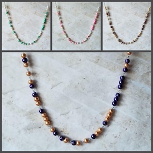 Könnte beinhalten: Drei Halsketten mit unterschiedlich farbigen Perlen. Die erste Halskette hat grüne und weiße Perlen, die zweite hat rosa und weiße Perlen und die dritte hat braune und weiße Perlen. Die vierte Halskette hat lila und goldene Perlen.