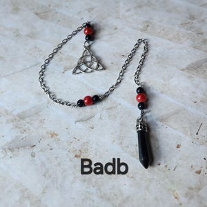 Peut inclure: Un pendule à chaîne argentée avec une pointe en cristal noir. La chaîne comporte des perles rouges et noires et un charme de nœud celtique. Le mot "Badb" est imprimé en noir au bas de l'image.