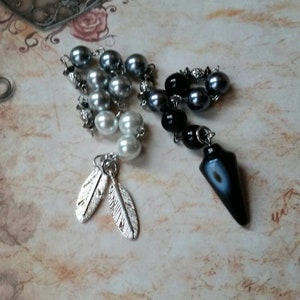 May include: A silver and black beaded pendulum with a black and white agate point. The pendulum is attached to a silver chain with two silver feather charms.