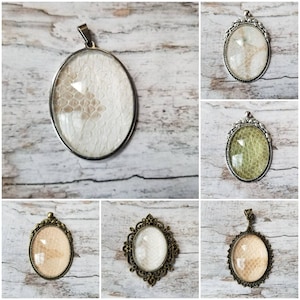 May include: Six different oval-shaped pendants with ornate silver and bronze frames. The pendants feature a variety of textures and patterns, including a white snakeskin pattern, a green snakeskin pattern, and a clear glass pattern.