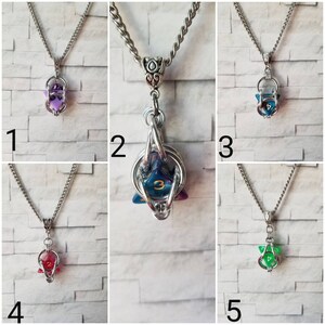 Puede incluir: Cinco collares con una cadena de plata y un colgante de jaula de plata. Cada jaula contiene un dado d20 de color diferente. Los dados son morado, azul, verde, rojo y transparente con acentos azules y morados.