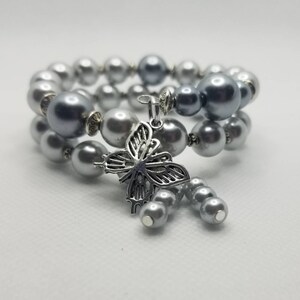 May include: A silver and gray beaded bracelet with a silver butterfly charm. The bracelet is made of two strands of beads and has a magnetic clasp.