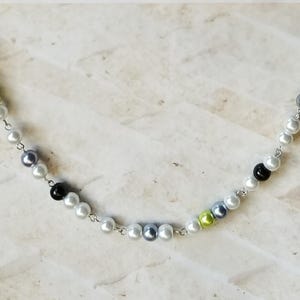 Puede incluir: Un collar de cadena de plata con cuentas de perlas blancas, negras y verdes.