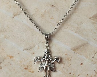 May include: A silver-toned pendant necklace featuring a stylized female figure with wings and holding objects in each hand. The pendant is suspended from a delicate chain. The figure has detailed features and is set against a neutral background.