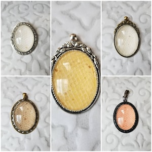May include: Four oval-shaped pendants with different colored resin inserts. The pendants are silver-toned with ornate designs.