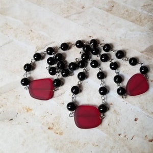May include: A black beaded necklace with three red glass pendant charms. The necklace is made of small black beads and silver chain.