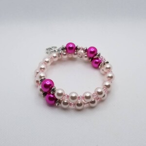 K&ouml;nnte beinhalten: Ein Armband mit zwei Reihen aus rosa und wei&szlig;en Perlen. Das Armband hat einen silbernen Anh&auml;nger.