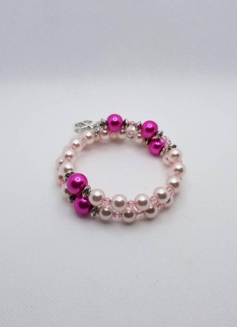 K&ouml;nnte beinhalten: Ein Armband mit zwei Reihen aus rosa und wei&szlig;en Perlen. Das Armband hat einen silbernen Anh&auml;nger.
