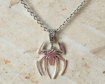 Pode incluir: Colar com pingente de aranha prateada. O pingente apresenta um design de aranha estilizado com pernas longas e curvas e um corpo detalhado. A corrente do colar é de estilo elo delicado, e o pingente pende de uma fiança decorativa.