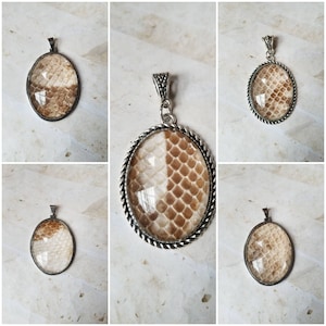 May include: Four silver pendants featuring a brown and white snakeskin pattern inside. The pendants are oval shaped and have a silver chain attached.