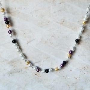 Puede incluir: Un collar de cadena plateada con cuentas blancas, negras y moradas.