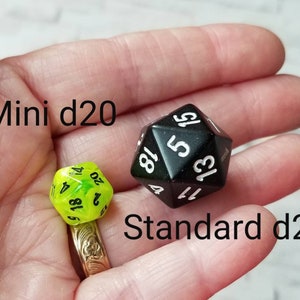 May include: A close-up of two black and white twenty-sided dice, one mini and one standard size. The mini die is green and translucent. The standard die is black and opaque. The text "Mini d20" and "Standard d20" is visible in the image.