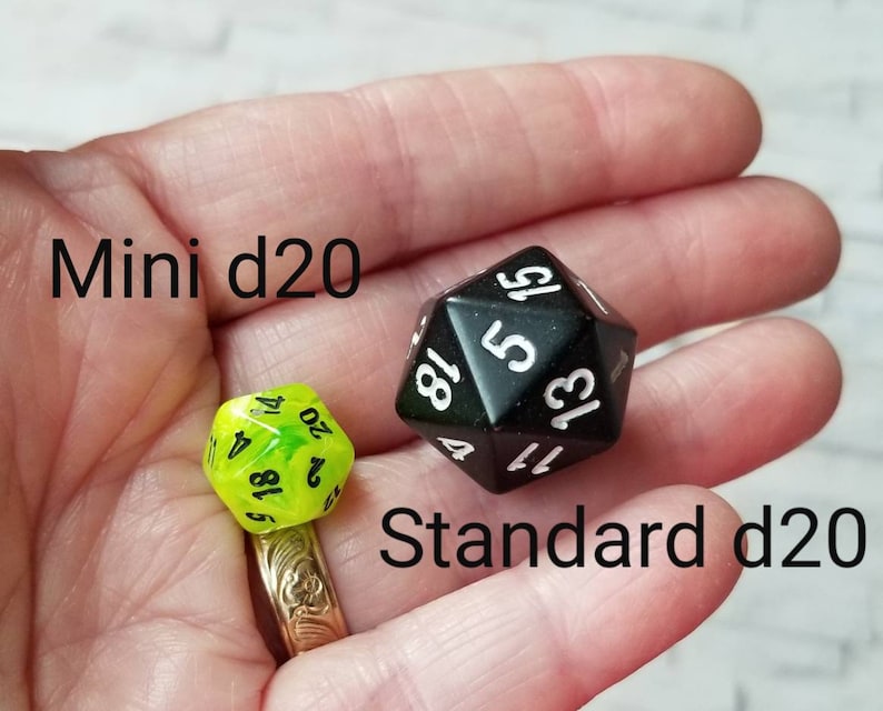 May include: A close-up of two black and white twenty-sided dice, one mini and one standard size. The mini die is green and translucent. The standard die is black and opaque. The text "Mini d20" and "Standard d20" is visible in the image.