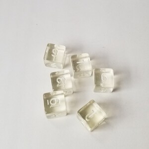 May include: Six clear plastic dice with white numbers on each side. The numbers are 1, 2, 3, 4, 5, and 6.