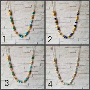 May include: Four necklaces with different color combinations of gold, blue, turquoise, and light green beads. The necklaces are displayed against a brick wall background.