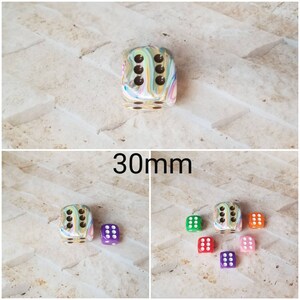 May include: A set of six 30mm dice in various colors, including green, red, purple, and pink. The dice are made of a marbled plastic material with white dots. The dice are arranged in a circle on a light gray surface.