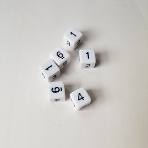 May include: Six white dice with black numbers. The dice show the numbers 1, 2, 3, 4, 5, and 6.