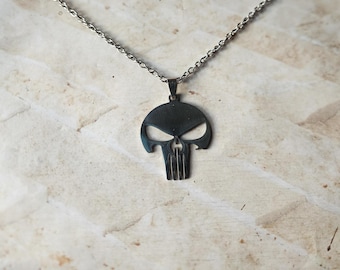 Pode incluir: Colar com pingente prateado com design de caveira. O pingente tem um formato de caveira estilizado com detalhes dos olhos e da boca. A corrente é de estilo elo delicado e o colar é exibido em um fundo neutro.
