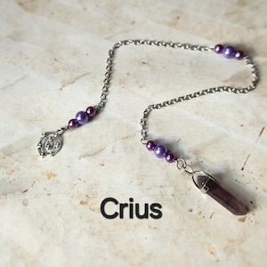 May include: A silver-colored chain with purple beads and a faceted amethyst crystal pendant. The chain also features a decorative silver charm. The word "Crius" is printed in black at the bottom of the image.
