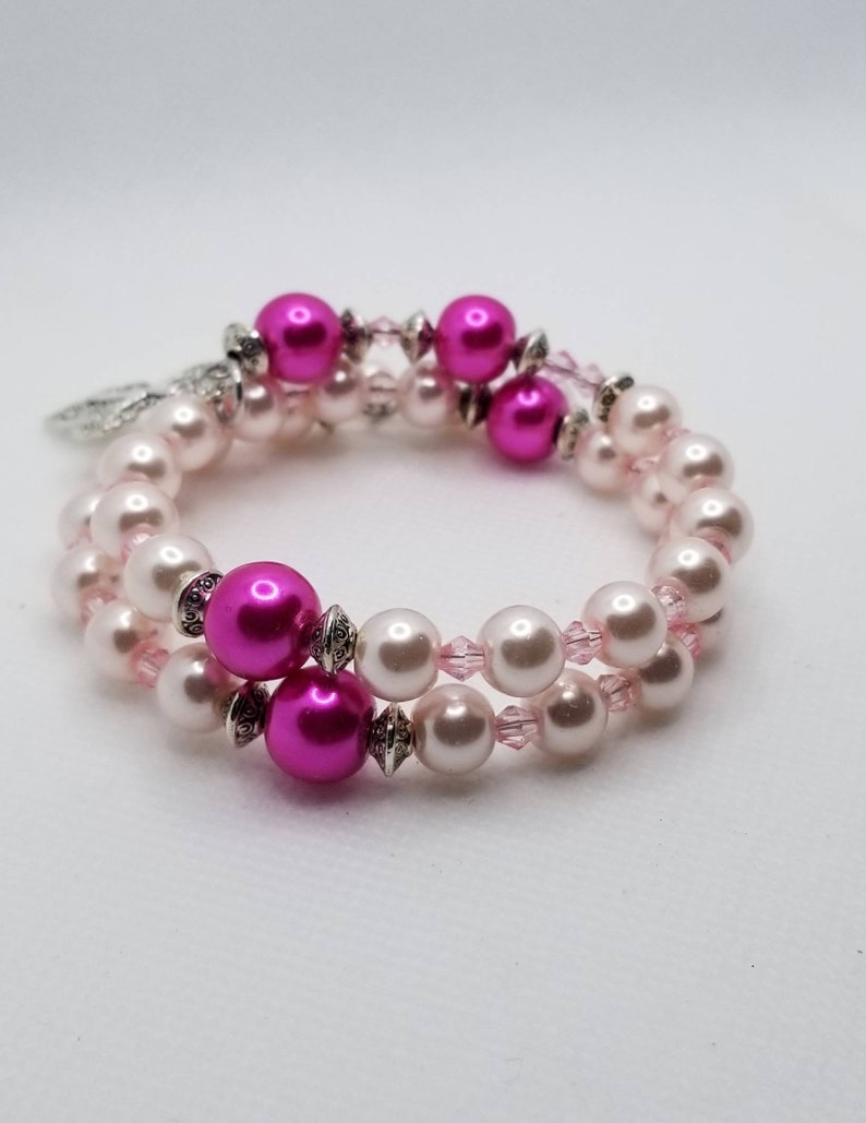 K&ouml;nnte beinhalten: Ein Armband mit zwei Reihen aus rosa und wei&szlig;en Perlen. Das Armband besteht aus rosa und silbernen Perlen mit einem silbernen Anh&auml;nger.