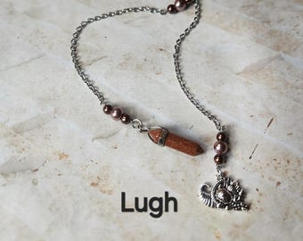 Puede incluir: Un marcapáginas de cadena plateada con un colgante de piedra preciosa marrón y un dije decorativo. El marcapáginas presenta cuentas marrones y la palabra "Lugh" en texto negro.