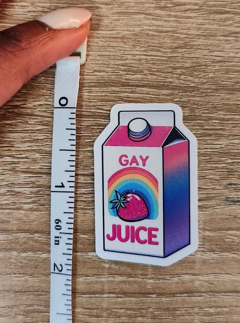 Puede incluir: Una pegatina blanca con una ilustraci&oacute;n de dibujos animados de un cart&oacute;n de jugo rosa y azul con un arco&iacute;ris y una fresa. El cart&oacute;n dice "Gay Juice" en texto negro.