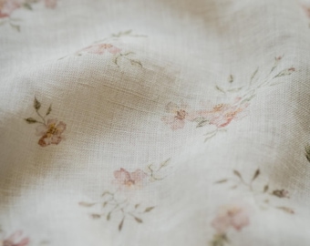 May include: A lightweight, off-white fabric featuring a delicate, repeating pattern of small, soft pink flowers with muted green leaves and stems. The material has a visible, slightly textured weave and is draped to show soft folds and shadows.