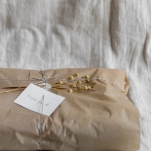 May include: A brown paper gift bag tied with twine and decorated with dried flowers. A white card with the text "Thank you" is attached to the bag.
