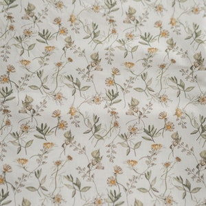 May include: A white fabric with a repeating pattern of small, light brown and yellow flowers and green leaves.