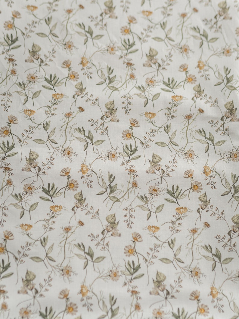 May include: A white fabric with a repeating pattern of small, light brown and yellow flowers and green leaves.